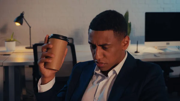Empresario afroamericano sosteniendo café para llevar en la oficina por la noche - foto de stock