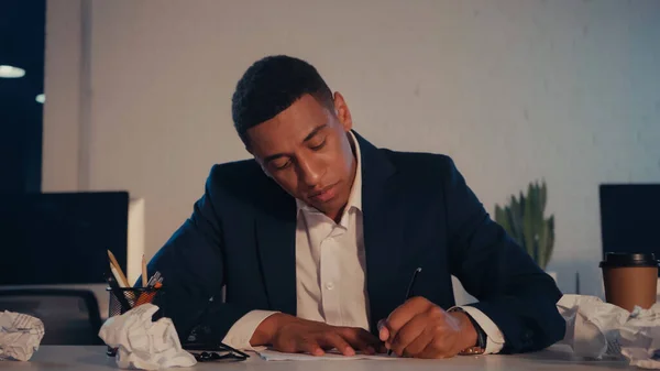 African american businessman writing on paper near coffee to go in office at night — Stock Photo