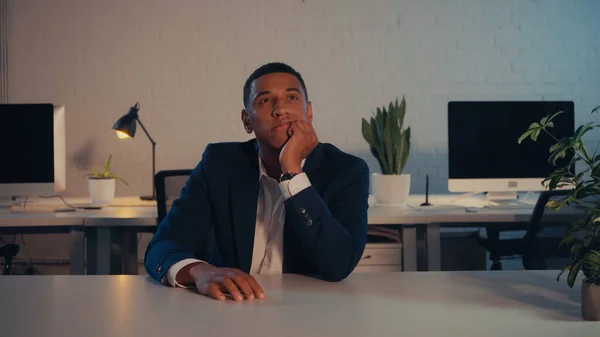 Thoughtful african american businessman sitting at table in office at night — Stock Photo