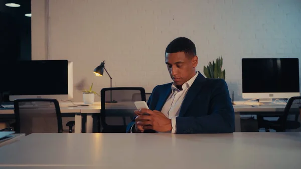 African american businessman in suit using cellphone in office at night — Stock Photo