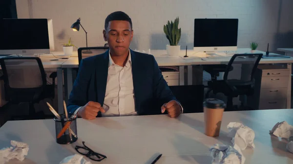 Wütender afrikanisch-amerikanischer Geschäftsmann im Anzug blickt auf zerknülltes Papier in der Nähe von Kaffee, um abends ins Büro zu gehen — Stockfoto