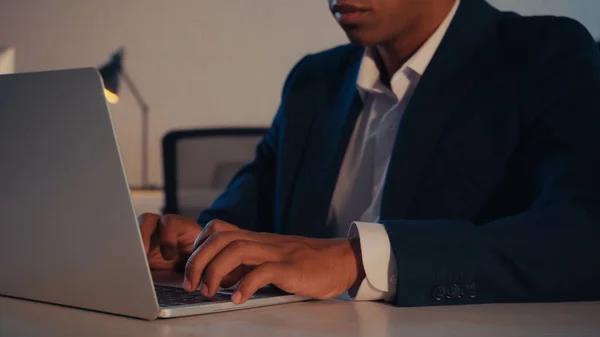 Cropped view of african american businessman using laptop in office in evening — Stock Photo