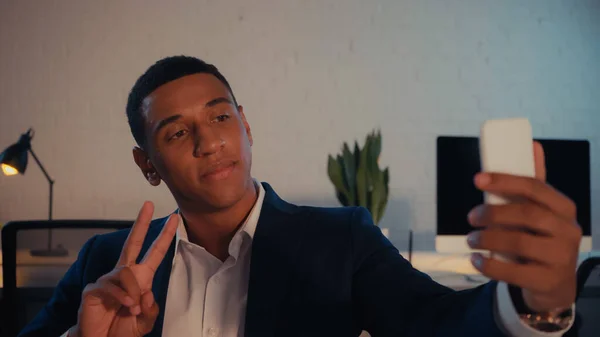 African american businessman showing peace sign white taking selfie on smartphone in office — Stock Photo