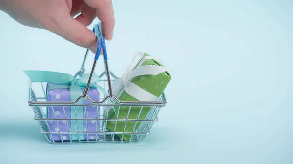 Partial view of man holding shopping basket with gifts on blue background — Stock Photo