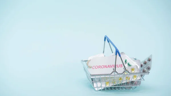 Small shopping basket with coronavirus lettering on card and medicaments on blue — Stock Photo