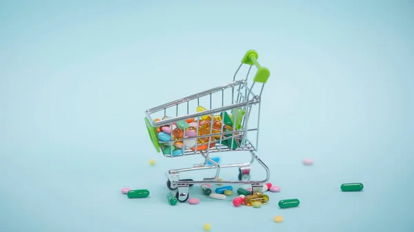 Píldoras coloridas dentro de la pequeña cesta de la compra sobre fondo azul - foto de stock