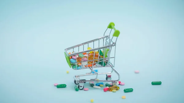 Colorful pills inside of small shopping cart on blue background — Stock Photo