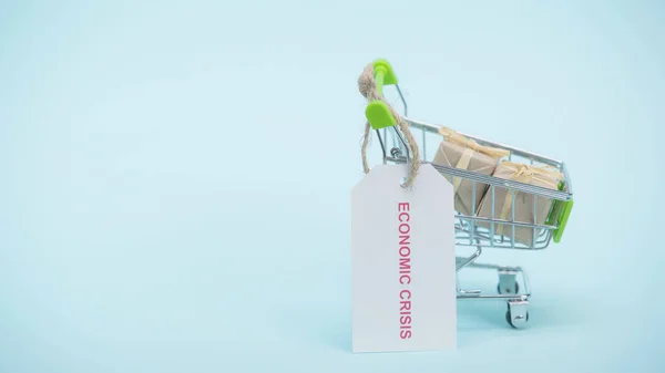 Pequeño carrito de compras con regalos y tarjeta con letras de crisis económica sobre fondo azul - foto de stock