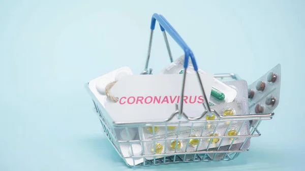 Cesta de la compra con letras coronavirus en la tarjeta y pastillas en azul - foto de stock