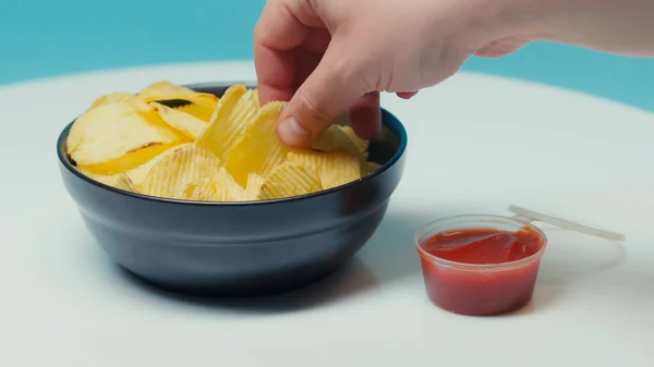 Vue recadrée de l'homme prenant croquants croustillants croustilles de pomme de terre sur bleu — Photo de stock