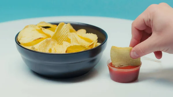Обрізаний вид людини, що занурює ковзані картопляні чіпси в кетчуп на синьому — стокове фото