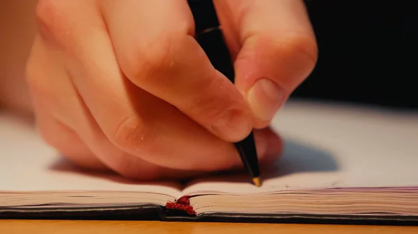 Vista cortada de homem segurando caneta enquanto escrevia em livro de cópia na mesa — Fotografia de Stock