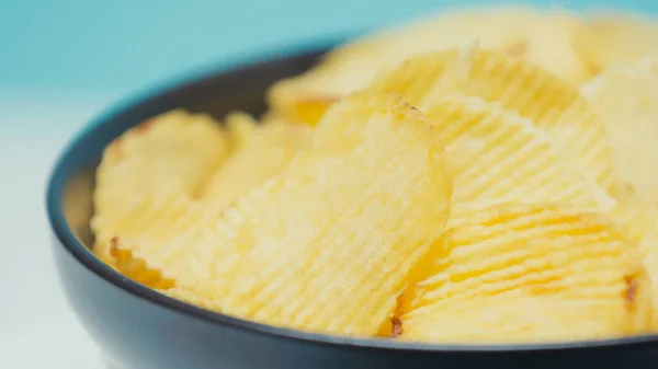 Крупним планом вид хрустких і рваних картопляних чіпсів в мисці на синьому — стокове фото