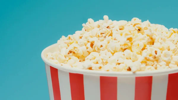 Delicious popcorn in big striped paper bucket isolated on blue — Stock Photo