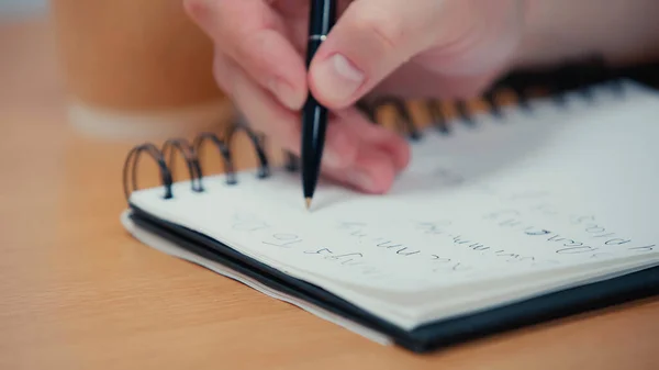 Visão cortada da pessoa segurando caneta e escrevendo em livro de cópia borrada — Fotografia de Stock
