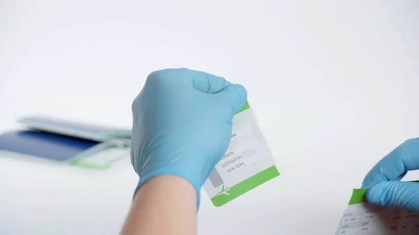 Partial view of person in latex gloves tearing boarding pass near blurred passport on white background — Stock Photo