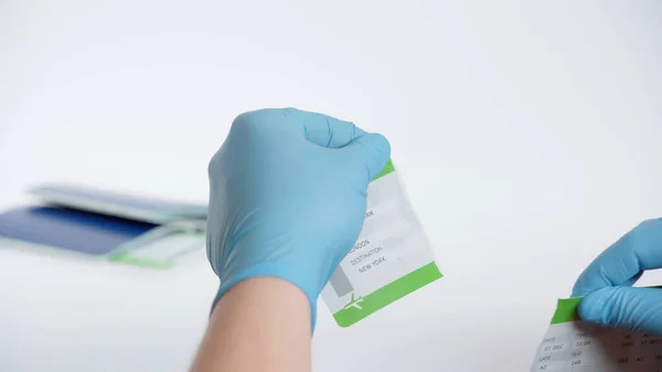 Vista parcial de la persona en guantes de látex rasgando la tarjeta de embarque cerca del pasaporte borroso sobre fondo blanco — Stock Photo