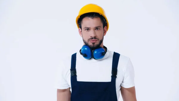 Seriöser Polier mit Helm und ohrenschützenden Kopfhörern, der auf weiß isoliert in die Kamera blickt — Stockfoto