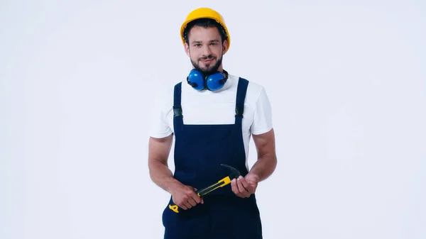 Joven reparador en mono y equipo de protección sosteniendo martillo aislado en blanco - foto de stock