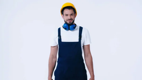 Jeune constructeur en salopette et casque souriant à la caméra isolé sur blanc — Photo de stock