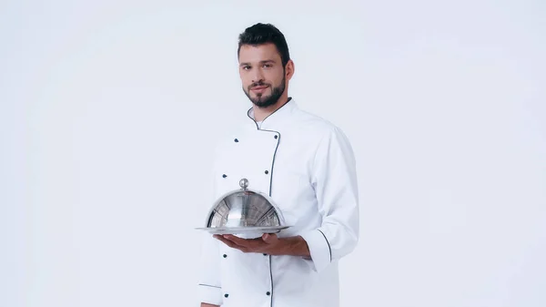 Young chef with serving dish and cloche looking at camera isolated on white — Stock Photo