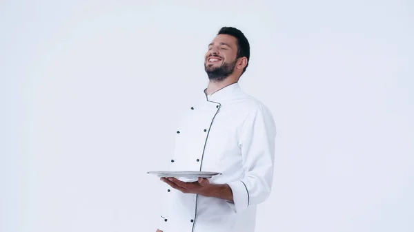 Веселий шеф-кухар із закритими очима тримає нержавіючу тарілку ізольовано на білому — стокове фото
