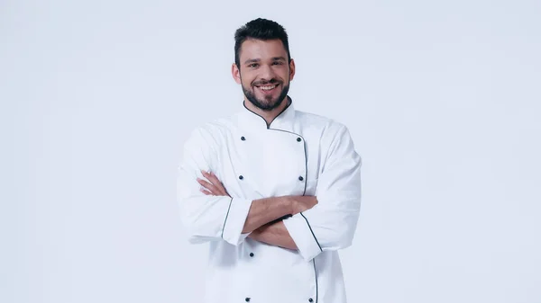 Young and happy man in chef jacket standing with crossed arms isolated on white — Stock Photo