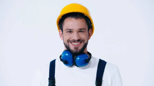 Fröhlicher Bauarbeiter mit geräuschunterdrückenden Kopfhörern und hartem Blick auf Kamera isoliert auf Weiß — Stockfoto