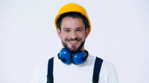 Allegro costruttore con cancellazione del rumore cuffie e hardhat guardando la fotocamera isolata su bianco — Foto stock