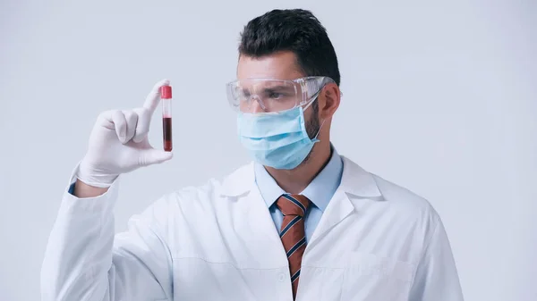 Virologist in goggles and medical mask holding blood sample in test tube isolated on grey — Stock Photo