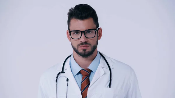 Бородатый доктор в очках и со стетоскопом, смотрящим на камеру, изолированную на сером — стоковое фото