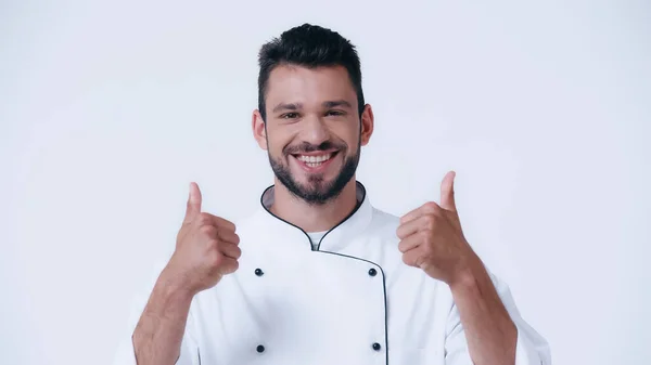 Щасливий молодий шеф-кухар показує великі пальці вгору і дивиться на камеру ізольовано на білому — стокове фото