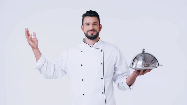 Alegre chef gesto mientras sostiene servir plato con cloche aislado en blanco - foto de stock