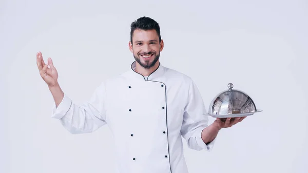 Jovem chef com placa de serviço e cloche inoxidável sorrindo para a câmera isolada em branco — Fotografia de Stock