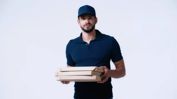 Молодой курьер в синей форме держит коробки от пиццы и смотрит на камеру, изолированную на белом — стоковое фото