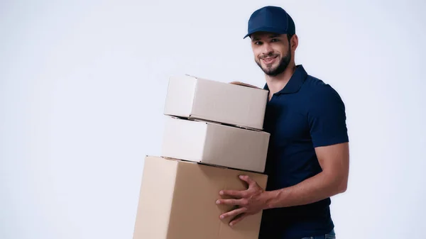 Repartidor sonriente llevando cajas de cartón aisladas en blanco - foto de stock