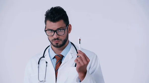 Médico morena en gafas que muestra termómetro electrónico aislado en gris - foto de stock