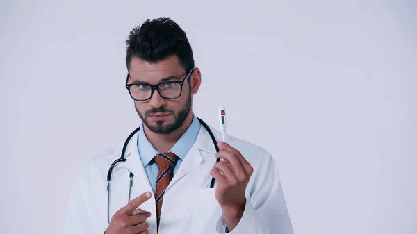 Médico serio con estetoscopio apuntando al termómetro electrónico aislado en gris — Stock Photo