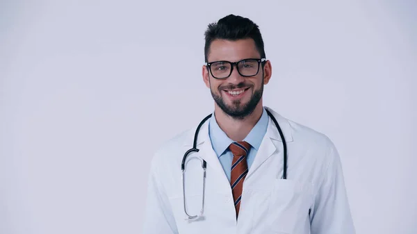 Cheerful young doctor in white coat and eyeglasses smiling at camera isolated on grey — Stock Photo