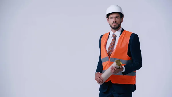 Arquitecto preocupado en chaleco de seguridad y hardhat celebración de tubo plano aislado en gris - foto de stock