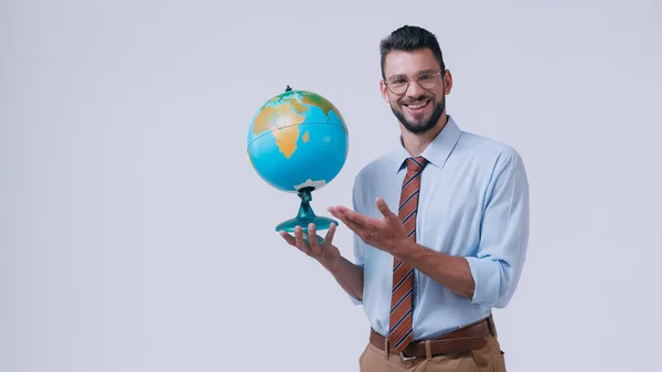 Positive teacher pointing at globe and looking at camera isolated on grey — Stock Photo