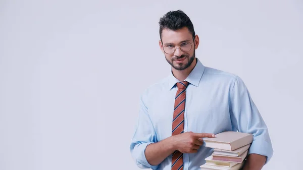 Junge Lehrerin mit Brille zeigt auf Stapel von Büchern isoliert auf grau — Stockfoto