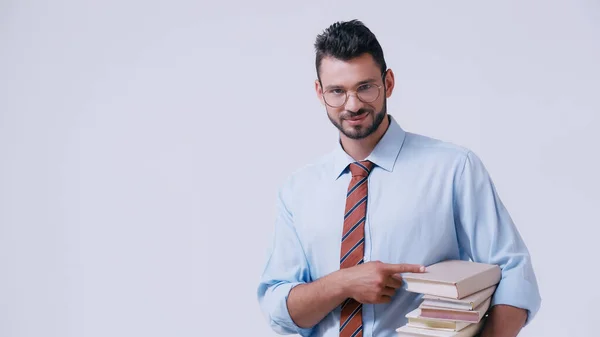 Giovane insegnante in occhiali che indica pila di libri isolati su grigio — Foto stock