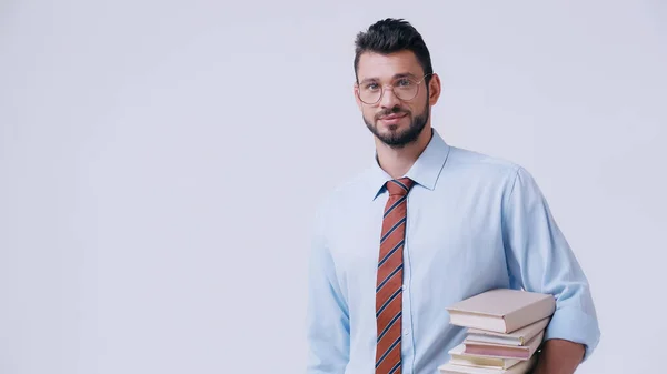 Young bearded teacher in eyeglasses holding stack of books isolated on grey — Stock Photo