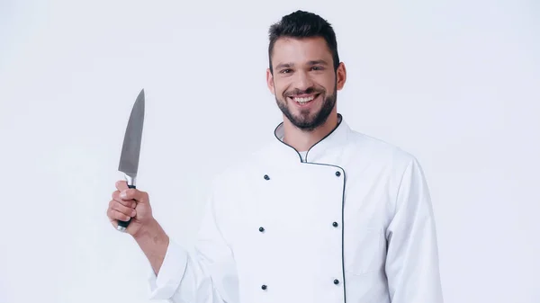 Alegre chef en uniforme sosteniendo cuchillo afilado y mirando a la cámara aislada en blanco - foto de stock