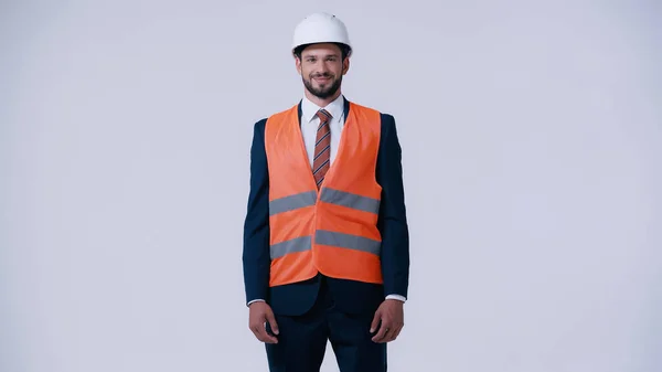 Happy architect in formal wear and protective equipment looking at camera isolated on grey — Stock Photo