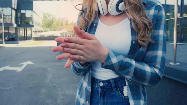 Обрізаний вид жінки з навушниками сушильний дезінфікуючий засіб на руках на відкритому повітрі — стокове фото