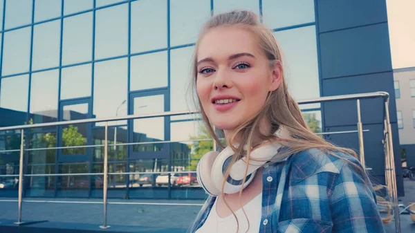 Молода жінка з бездротовими навушниками посміхається на камеру на міській вулиці — стокове фото