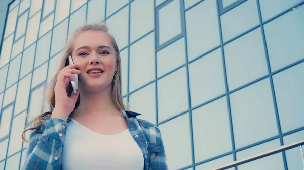 Vista a basso angolo della donna bionda che parla sul telefono cellulare sulla strada urbana — Foto stock