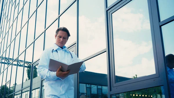 Врач просматривает документы в папке возле здания больницы — стоковое фото
